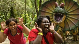 Two girls mock screaming with a dinosaur behind them